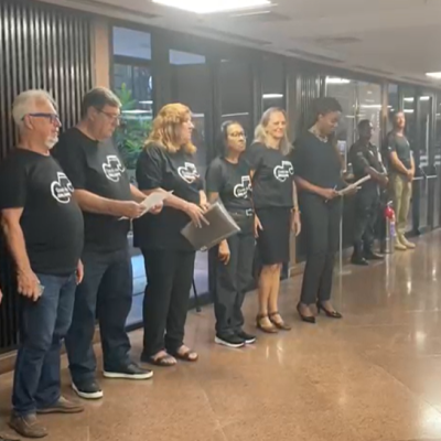 Maestro de frente para os integrantes do coral, todos vestidos de preto.