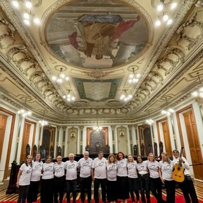 Foto posada dos integrantes, de calça preta e blusa branca, na sala de sessões, com destaque para a pintura da justiça no teto.